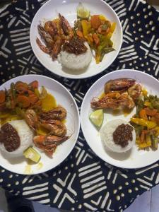La kora في Toubakouta: ثلاثة أطباق من الطعام مع الجمبري والخضروات على الطاولة