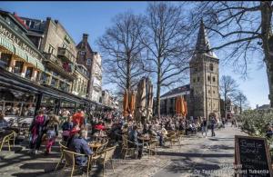 a crowd of people sitting at tables on a street with a clock tower at Hermanos City Appartement in Enschede