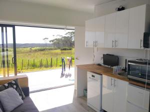 a kitchen with white cabinets and a view of a field at Seascape Peninsula Bach in Kaitaia