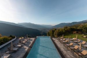 einen Pool mit Stühlen und Bergen im Hintergrund in der Unterkunft Panoramahotel Huberhof in Meransen