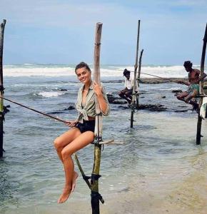 a woman sitting on a pole on the beach at Qiqi beach house in Weligama