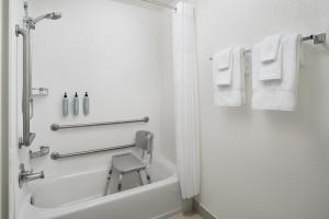 a bathroom with a shower and a chair next to a tub at Courtyard Baton Rouge South in Baton Rouge