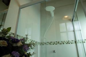 een douche met een glazen deur en een boeket bloemen bij Vila dos Caetés - Suíte 02 - Barra do Sahy in Barra do Sahy