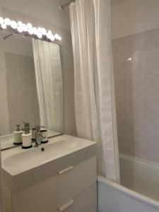 een badkamer met een wastafel, een spiegel en een bad bij Joli appartement avec parking et balcon in Touques