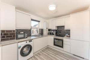 a kitchen with white cabinets and a washer and dryer at Luton flat near town centre for Relocators, Tourists, Families in Luton