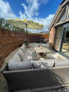 a wicker couch with a table and an umbrella at Luxury private FARM BARN, Airport, NEC 