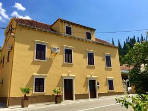 a yellow building with black shutters on a street at Rooms Mozara in Trsteno