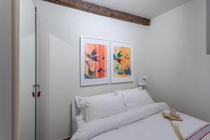 a white bedroom with a bed and paintings on the wall at La Casa di Enrichetta - Pavia City - by HOST4U in Pavia