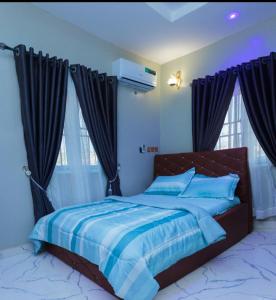 a bedroom with a bed with blue sheets and windows at D'EXQUISITE APARTMENTS in Ibadan