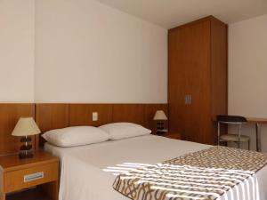 a bedroom with a bed and two tables and a chair at Flat e Suíte no Via Park - NF e Wi-FI in Campos dos Goytacazes