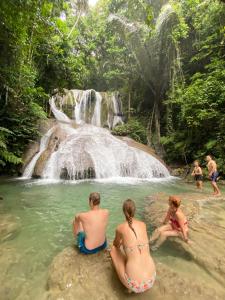 um grupo de pessoas sentadas na água em frente a uma cachoeira em Amadeo Guest House em Ratodena