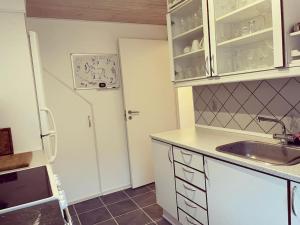 uma cozinha com armários brancos e um lavatório em Lejlighed med tagterrasse, have og pool. em Vipperød