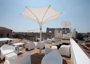 eine Dachterrasse mit weißen Stühlen, Tischen und einem Sonnenschirm in der Unterkunft Hotel Milano & SPA***S in Verona