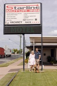 un hombre y una mujer y un perro de pie bajo una señal en Starline Motor Inn, en Miles