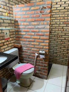 ein Badezimmer mit einer Ziegelwand und einem rosa Handtuch auf einem WC in der Unterkunft Casa do Ric in Caucaia