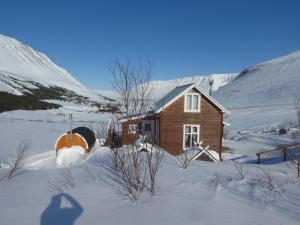 una pequeña casa en la nieve frente a una montaña en Valhöll Skátaskáli, en Ísafjörður