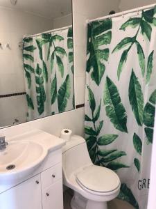 a bathroom with a toilet and a shower curtain with leaves at Condominio costazul La Herradura in Coquimbo