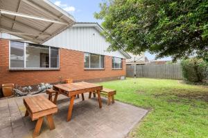 a patio with a wooden table and benches in a yard at Lonnie Getaway in Point Lonsdale
