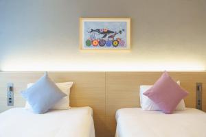 two beds with pillows in a hotel room with a picture at 琉球オリオンホテル 那覇国際通り in Naha