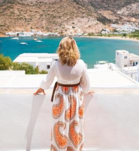 a woman standing on a ledge looking at the ocean at Sifnos House - Rooms and SPA in Kamarai