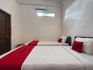 two beds in a room with red and white at RedDoorz Syariah at Falisha UMY in Ngabean