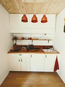 Aux Trois Chênes Lodge Spa في ميرْكو: مطبخ مع خزائن بيضاء وأضواء برتقالية