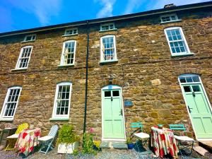 an old stone house with green doors and chairs at Castle Buildings Cottage2 in Llanrhaeadr-ym-Mochnant