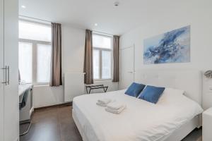 a white bed with blue pillows in a room with windows at Maison Bruges in Bruges