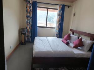 - une chambre avec un lit doté d'oreillers roses et d'une fenêtre dans l'établissement Bunyonyi Lakefront Leisure Lodge, à Kabale