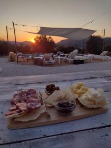 una tabla de cortar con comida en una mesa con la puesta de sol en Pasare Glamping_AnglonaRuralExperience, en Perfugas
