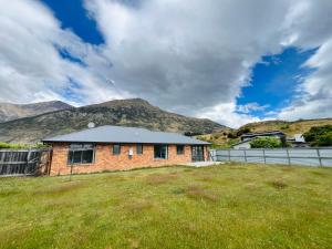 a brick house in a field with mountains in the background at Leisure Holiday Home Lake Hayes Easte Queenstown in Arrowtown