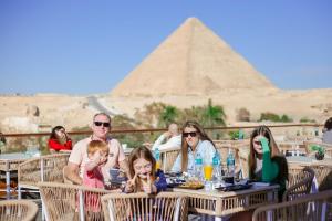un groupe de personnes assises à une table devant les pyramides dans l'établissement Tree Lounge Pyramids View INN , Sphinx Giza, au Caire