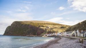 a beach with houses next to the water and a mountain at The Wee House in Pennan