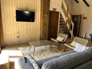 sala de estar con sofá, sillas y TV en Cabañas Wildki Lodge Vichuquen, en Curicó