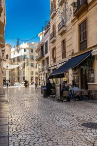 una calle adoquinada con gente sentada en las mesas en Strachan Apartamentos en el corazón de Málaga, en Málaga