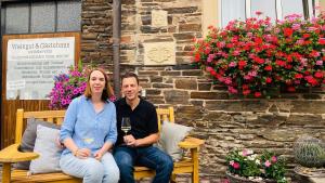 a man and woman sitting on a bench with a glass of wine at Gästehaus Kiebel in Lösnich
