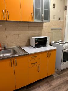een keuken met oranje kasten, een wastafel en een magnetron bij Сеть BRAUN Сатпаева 11 in Pavlodar