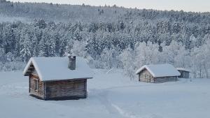 Deux petits bâtiments sont recouverts de neige et d'arbres dans l'établissement Leppälän vanhatupa rantasaunalla, à Utsjoki