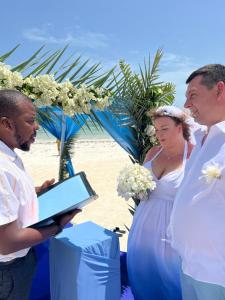 Una novia y un novio en la playa con un hombre sosteniendo una tableta en Gadea Boutique Hotel& Gadea Garden Italian Restaurant en Jambiani