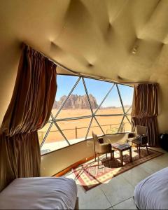 Habitación con ventana grande, escritorio y mesa. en RUM ROYAL FLOWER lUXURY CAMP en Wadi Rum