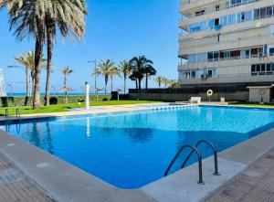 a swimming pool with palm trees and a building at Apartamento 1ª LINEA PLAYA MUCHAVISTA in El Campello