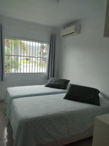 two beds in a white room with a window at Casa de praia na Gamboa - Garopaba SC in Garopaba