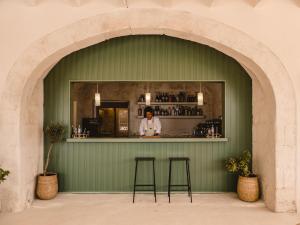 Eine Frau, die hinter einer grünen Bar mit zwei Hockern steht. in der Unterkunft Hotel Rural Morvedra Nou in Ciutadella