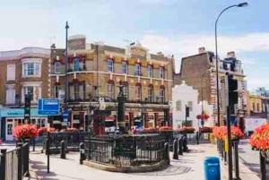 a city street with buildings and flowers in front at Hidden Oasis Comfy Studio in New Cross London in London