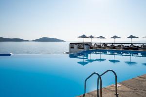 uma piscina com água azul e guarda-sóis em Aquila Elounda Village Resort, Suites & Spa em Elounda