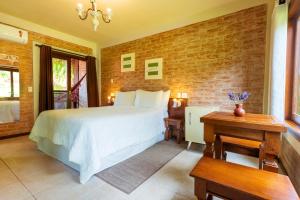 a bedroom with a white bed and a brick wall at Pousada Boutique Vilage de Minas in Monte Verde
