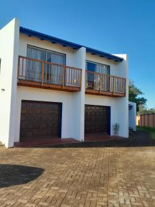 a white house with two garage doors and a balcony at Indaba Manor Guesthouse in Port Edward