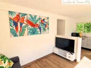 ein Wohnzimmer mit einem TV und Gemälden an der Wand in der Unterkunft La Villa du Toucan d'Or, au cœur de la Guadeloupe in Petit-Bourg