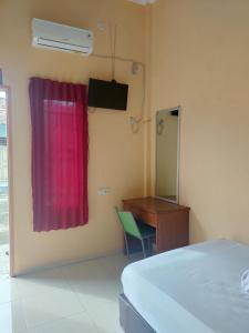 a bedroom with a bed and a desk and a red curtain at Serasikost in Sukarami