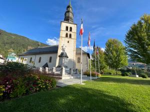a church with a tower with flags in the grass at un nid avec balcon in Saint-Gervais-les-Bains
